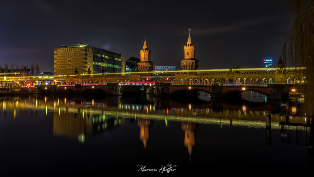 Die Oberbaumbrücke in Berlin bei Nacht, die Lichter spiegeln sich in der Spree