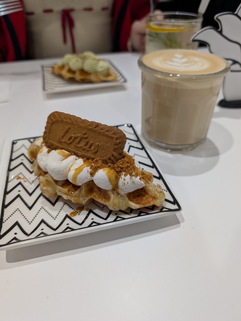 Auf einem Teller liegt eine Biscuit Croffle (Mix aus Croissant und Waffel) sowie ein Glas Latte Macchiato